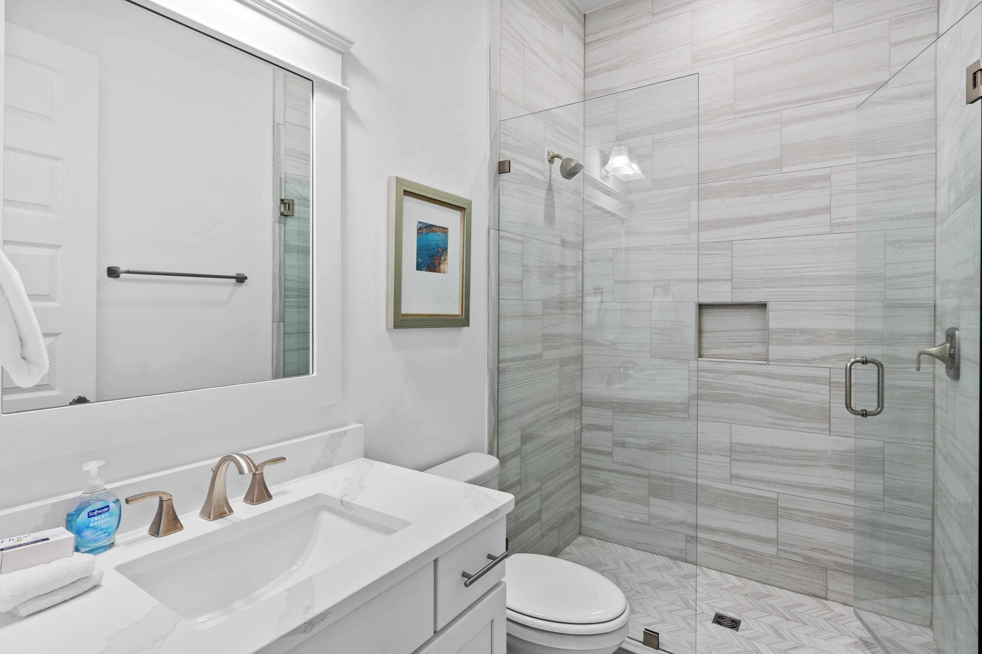 A modern bathroom with a large mirror, a white sink with a marble countertop, a toilet, and a glass-enclosed shower area.