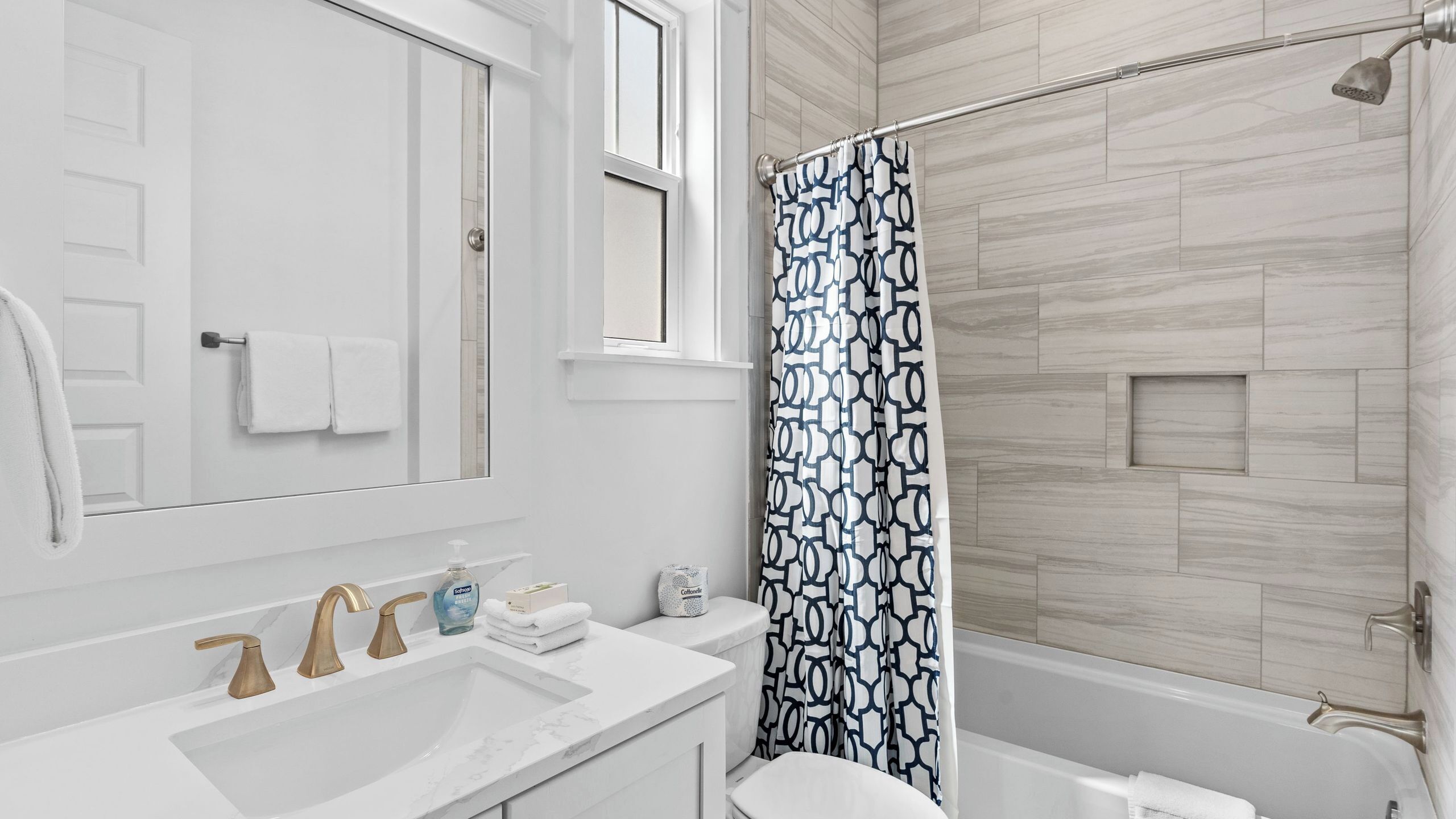 Un bagno con doccia, un lavandino a due rubinetti, un water e uno specchio.
