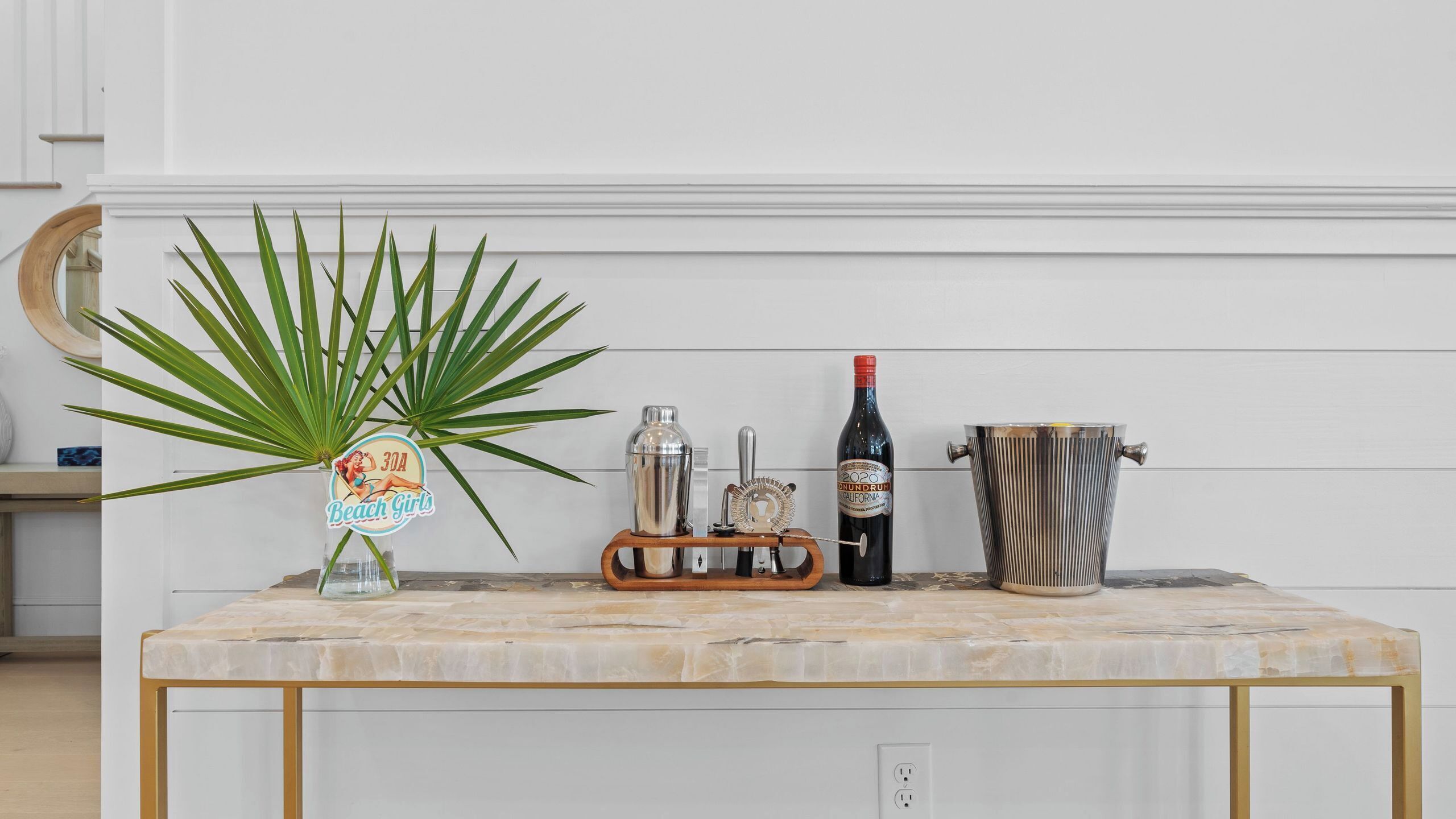 A bar area with a marble countertop, a cocktail shaker, a bottle of wine, a metal bucket, and a plant.