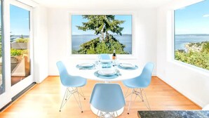 Ein Essbereich mit Tisch für vier Personen, großen Fenstern mit Blick auf die Küste und einem modernen Interieur.