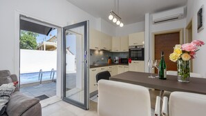 Una cucina moderna con zona pranzo, una porta scorrevole in vetro verso una piscina esterna e un vaso di fiori sul tavolo.