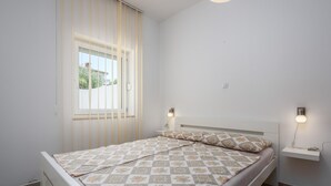 A bedroom with a bed, a window with blinds, a bedside table with a lamp, and a wall-mounted shelf. - Apartment in Kukci With Heated Pool (Porec)