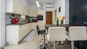 Una cucina moderna con mobili bianchi e beige, una macchina da caffè rossa e un'area pranzo con due sgabelli da bar bianchi.