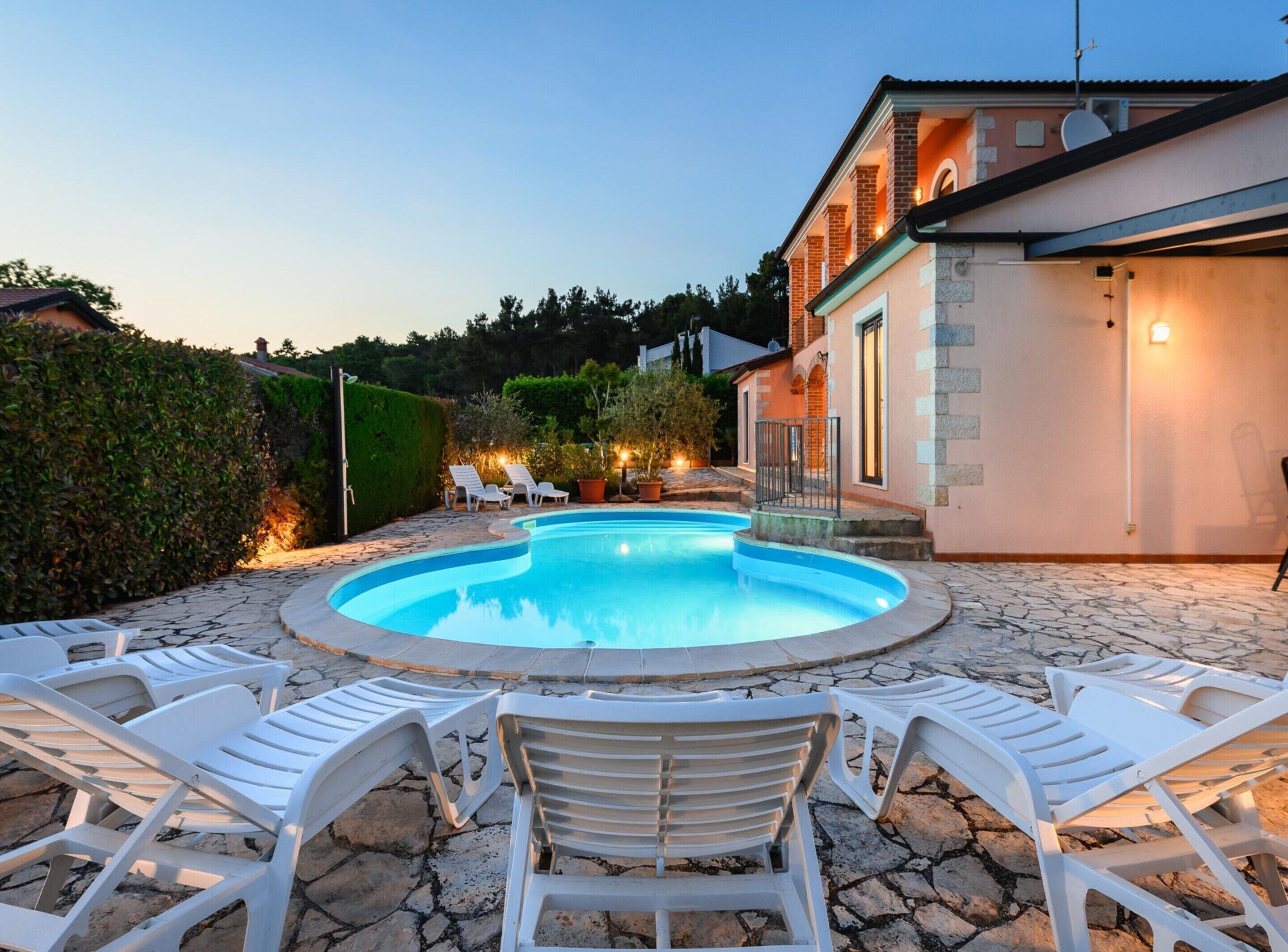 A swimming pool with lounge chairs, a stone patio, and a building with a light-colored exterior.