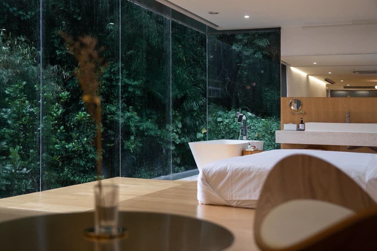 A modern bedroom with a large window, a bathtub, and a view of mountains.