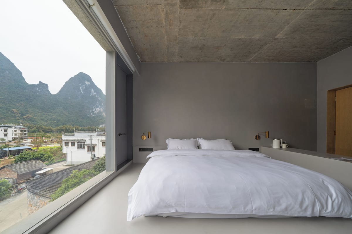 A bedroom with a large bed, a view of mountains, and a cityscape.