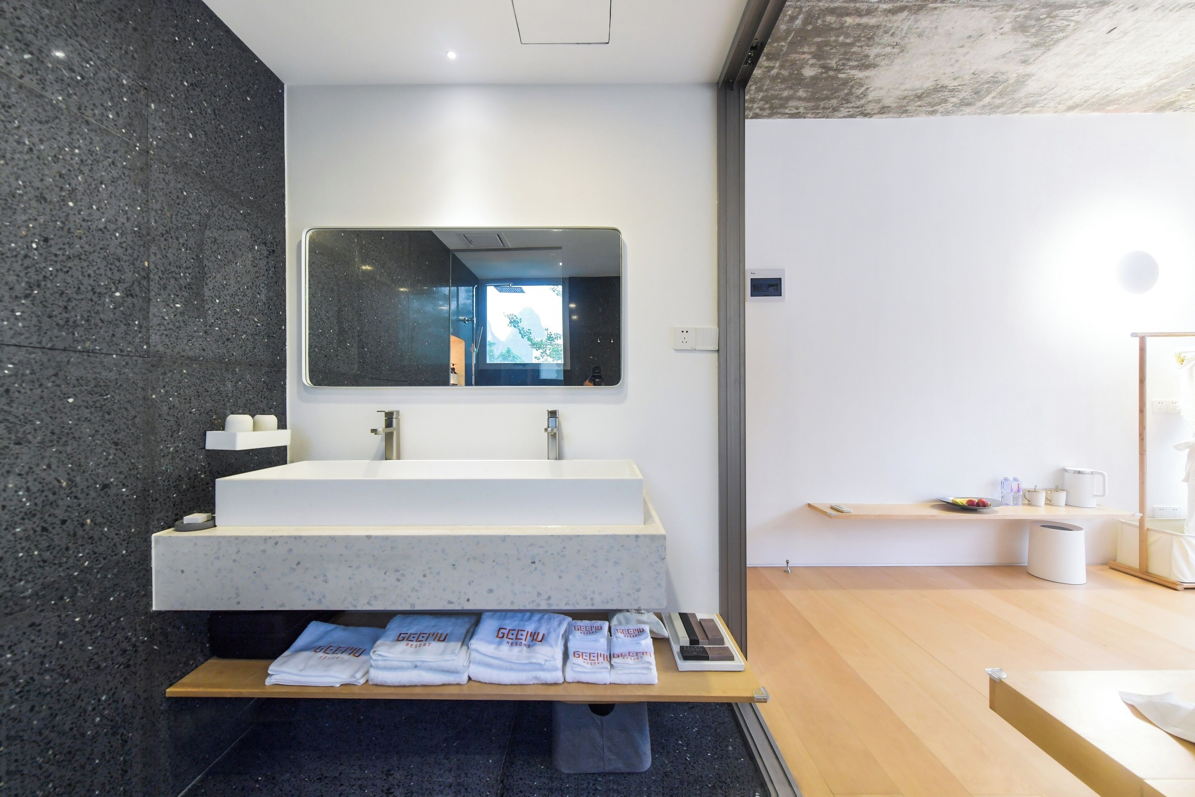 A modern bathroom with a large mirror, a freestanding sink, and a wooden bench with towels.