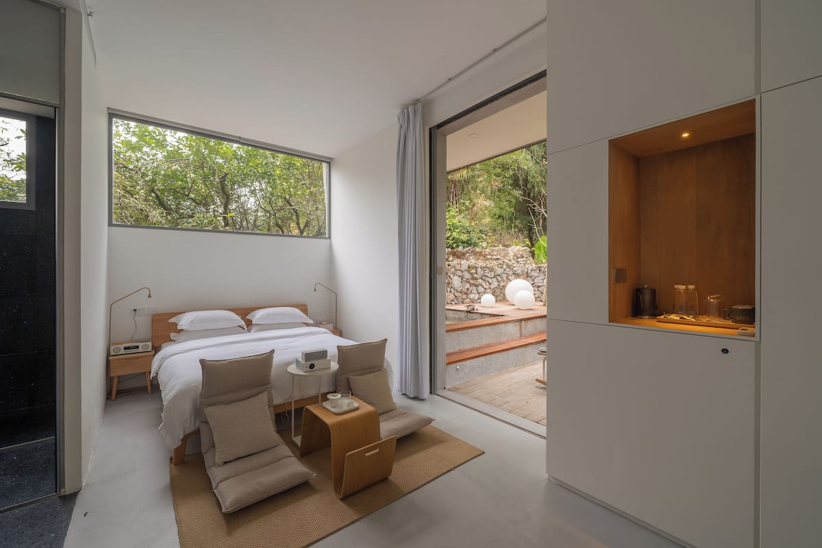 A modern bedroom with a bed, bedside tables, and a view of the outdoors.