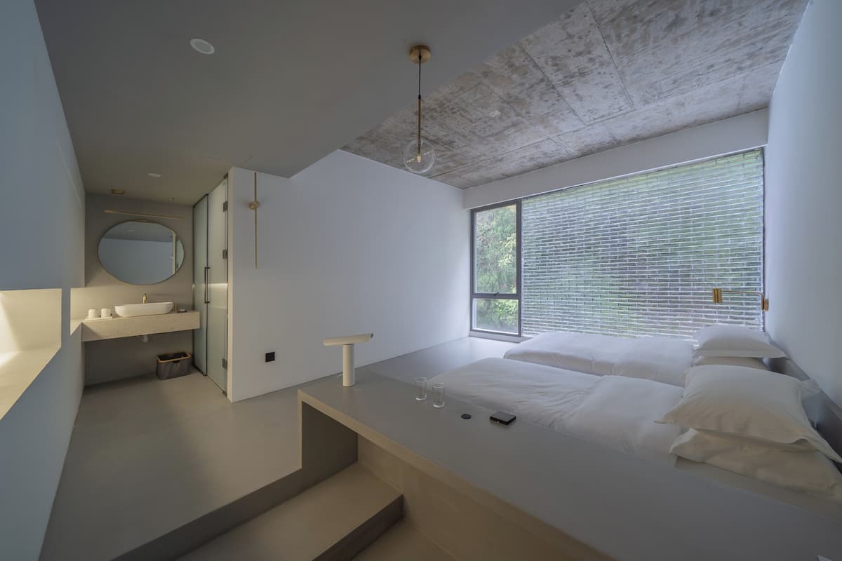 A modern bedroom with a large window, a built-in desk, and a minimalist design.