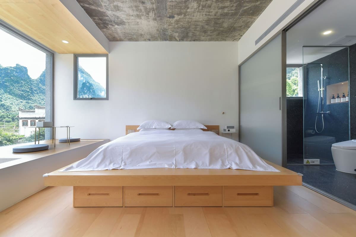 A modern bedroom with a wooden bed, a view of mountains, and a glass shower area.