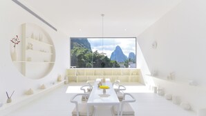 A modern dining area with a white table and chairs, a large window with a mountain view, and white shelves with decorative items. - Yangshuo Geemu Building House (Guilin)