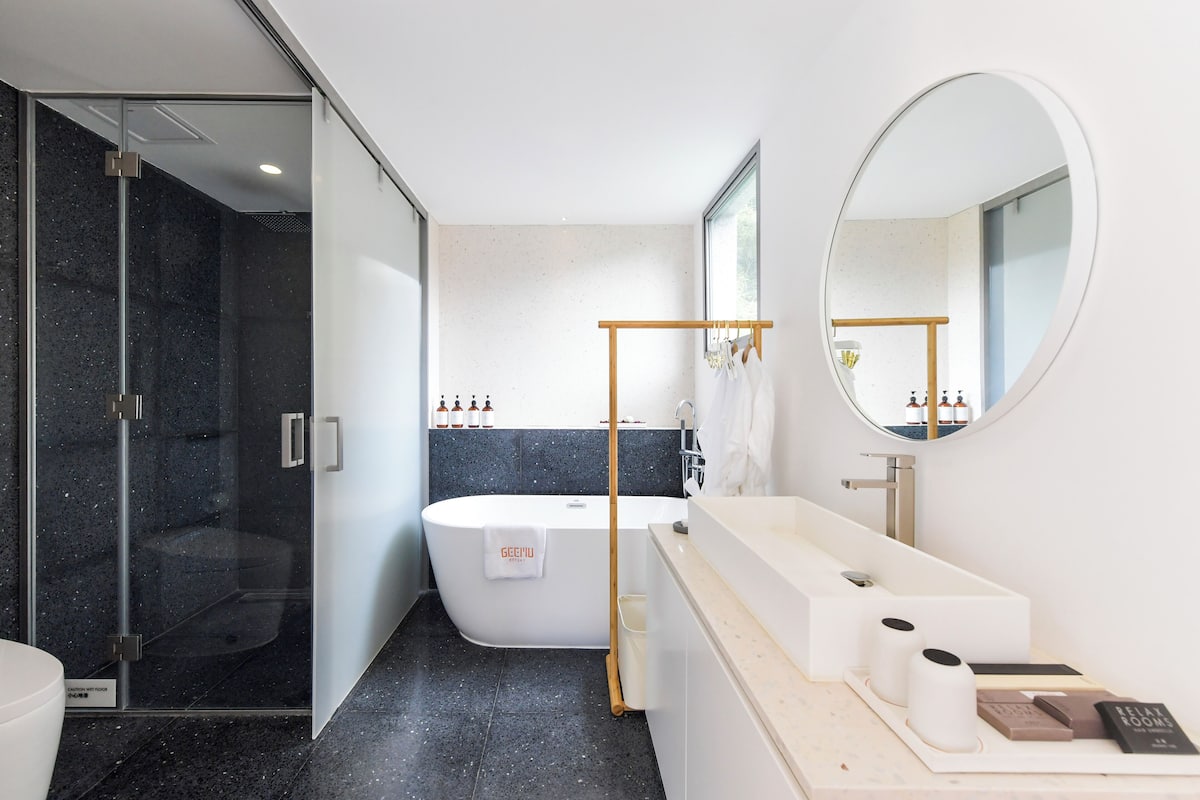 A modern bathroom with a glass shower enclosure, a freestanding bathtub, and a vanity with a mirror.