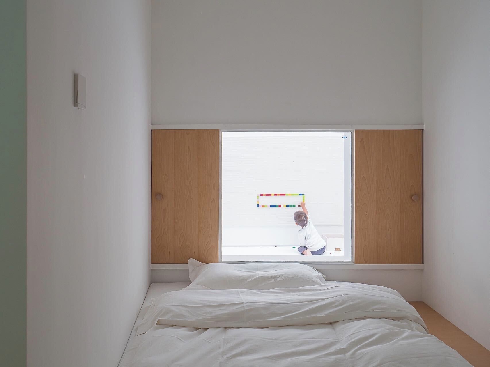 A bedroom with a large window, a bed with white bedding, and wooden paneling on the walls.