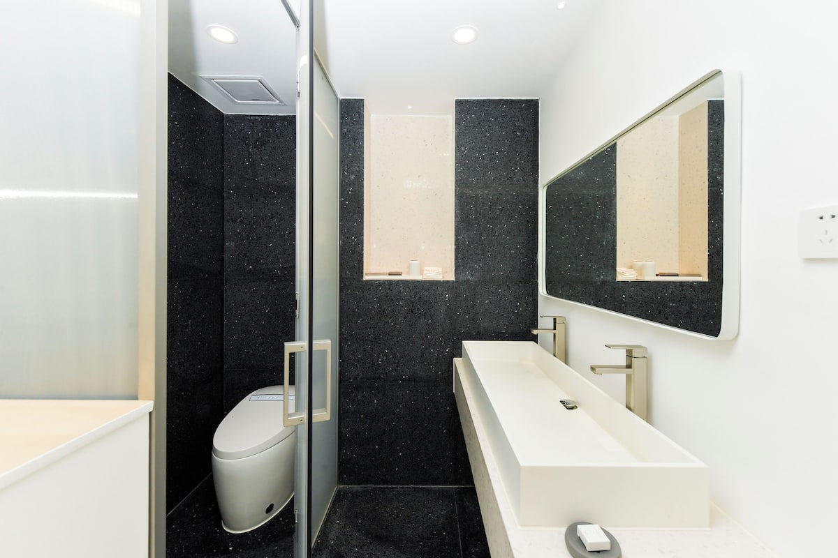 A modern bathroom with a white sink, a large mirror, and a toilet.