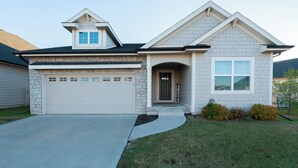 A two-story house with a garage, a small porch, and a landscaped front yard. - The Rehoboth- Iowa -Entire Home, 4BR- Deluxe & Elegant, Great Location near I-35 (Ankeny)