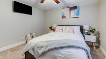 Ein Schlafzimmer mit Bett, Nachttischen, Deckenventilator, Flachbildfernseher und zwei Wandbildern.