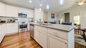 A modern kitchen with white cabinets, stainless steel appliances, and a central island with a sink. - The Rehoboth- Iowa -Entire Home, 4BR- Deluxe & Elegant, Great Location near I-35 (Ankeny)