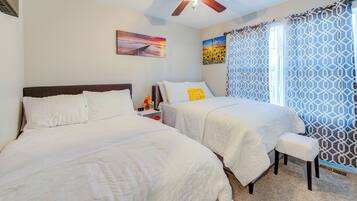 A bedroom with two beds, a ceiling fan, and artwork on the walls.