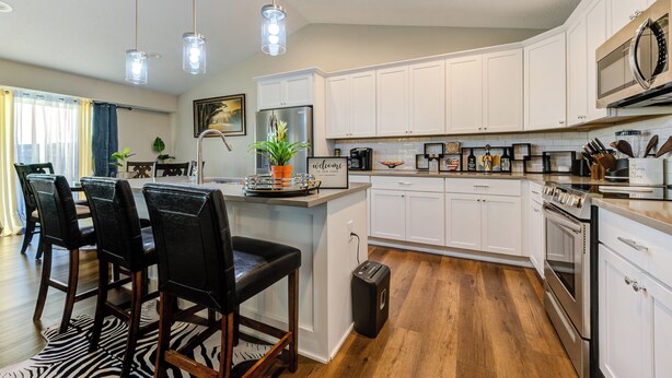 A modern kitchen with white cabinets, a stainless steel refrigerator, and a built-in oven. There is a dining area with a zebra-patterned rug and black chairs. - The Rehoboth- Iowa -Entire Home, 4BR- Deluxe & Elegant, Great Location near I-35 (Ankeny)