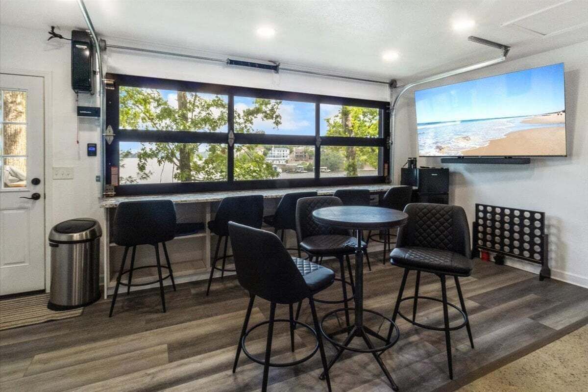 A room with a large window, a TV mounted on the wall, and several black chairs and tables.