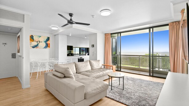 Ein modernes Wohnzimmer mit einem beigen Sofa, einer Essecke mit weißen Stühlen und einem großen Balkon mit Blick.