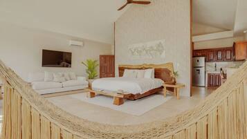 A spacious bedroom with a large bed, a ceiling fan, a view of the kitchen, and a hammock in the corner.