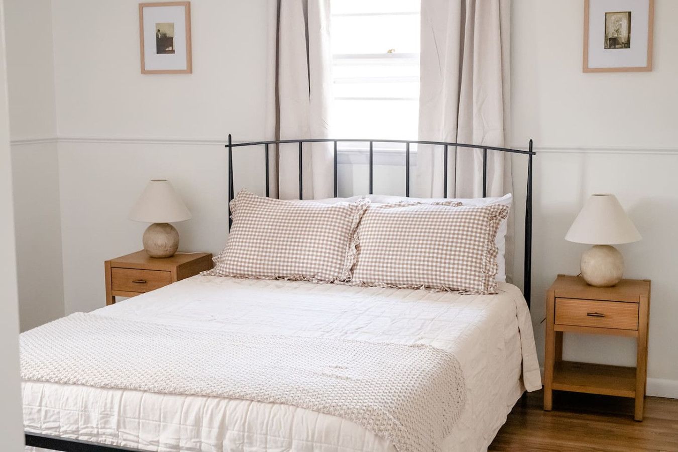 A neatly made bed with a checkered pillow and two bedside tables with lamps.