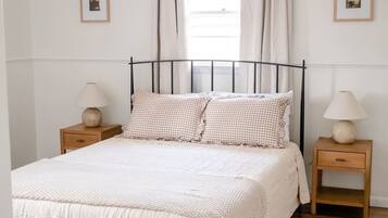 A neatly made bed with a checkered pillow and two bedside tables with lamps.