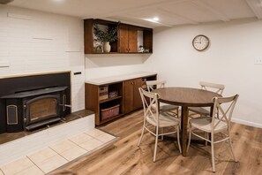 Una cocina con horno empotrado, armarios de madera, una mesa de comedor con sillas y un reloj de pared.