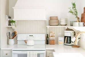 Uma cozinha moderna com armários brancos, fogão embutido, cafeteira e diversos utensílios de cozinha.