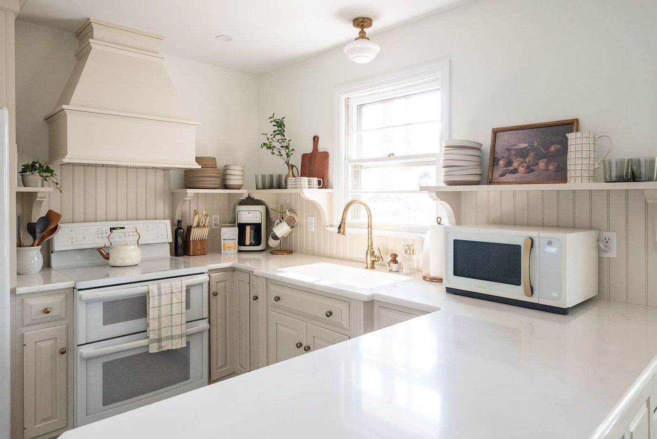 A kitchen with white cabinetry, a built-in oven, a microwave, a sink with a gold faucet, and various kitchen utensils and appliances.