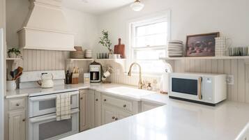A kitchen with white cabinetry, a built-in oven, a microwave, a sink with a gold faucet, and various kitchen utensils and appliances.