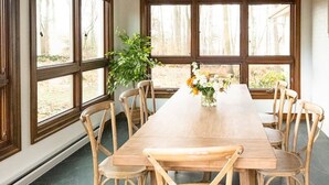 Un espace repas comprenant une longue table en bois, six chaises en bois et de grandes fenêtres donnant sur la forêt.