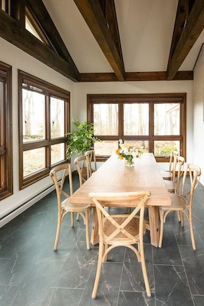 Un comedor con una larga mesa de madera, seis sillas de madera y ventanas grandes que dan a unas árboles.
