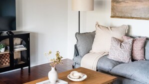 Un salon avec un canapé gris, une table basse en bois, un vase blanc contenant des fleurs séchées et une lampe.