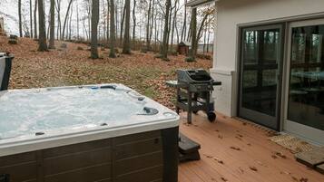 A hot tub on a wooden deck with a grill and a glass door leading to a covered patio.