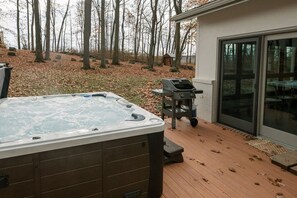 Jacuzzi en terraza de madera con una parrilla y puerta de vidrio que da a un porche cubierto.