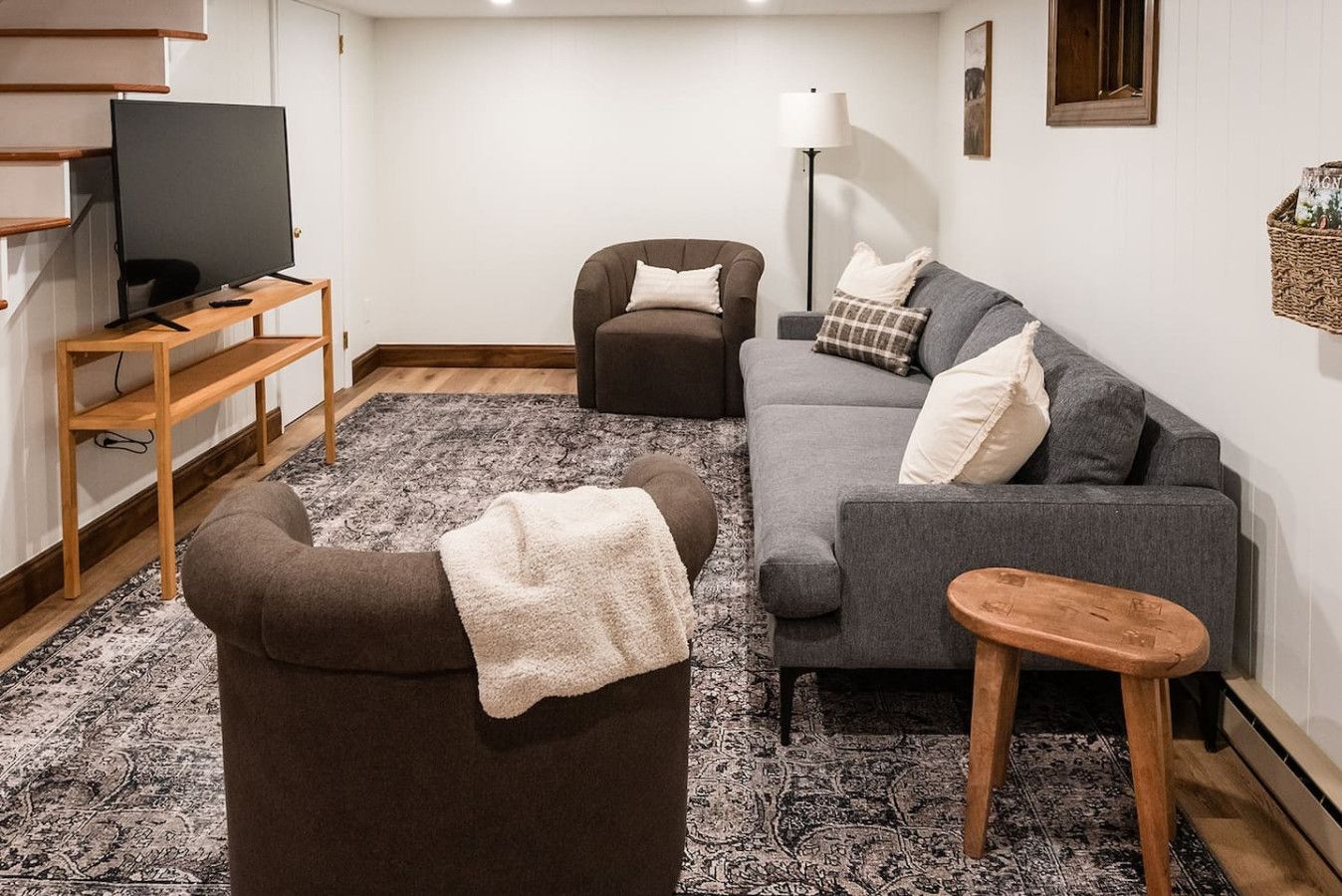 A living room with a sofa, armchair, TV on a stand, and a floor lamp.
