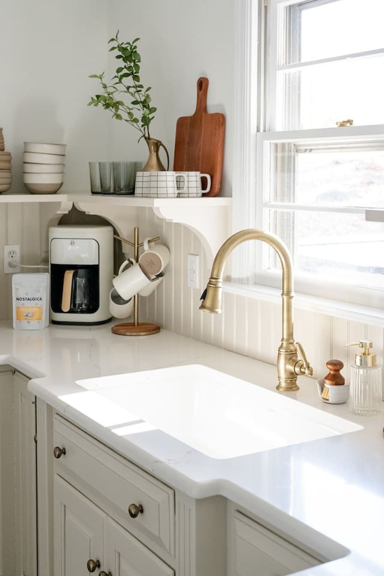 Eine Küche mit weißer Arbeitsplatte, einem goldenen Wasserhahn und einer Kaffeemaschine.