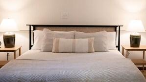 Un lit bien fait, recouvert d’une couverture à motifs, deux tables de chevet avec des lampes et une tête de lit ornée d’un motif tissé.