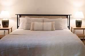 Una cama bien hecha con un edredón texturizado, dos mesitas de noche con lámparas y un cabecero con diseño tejido.