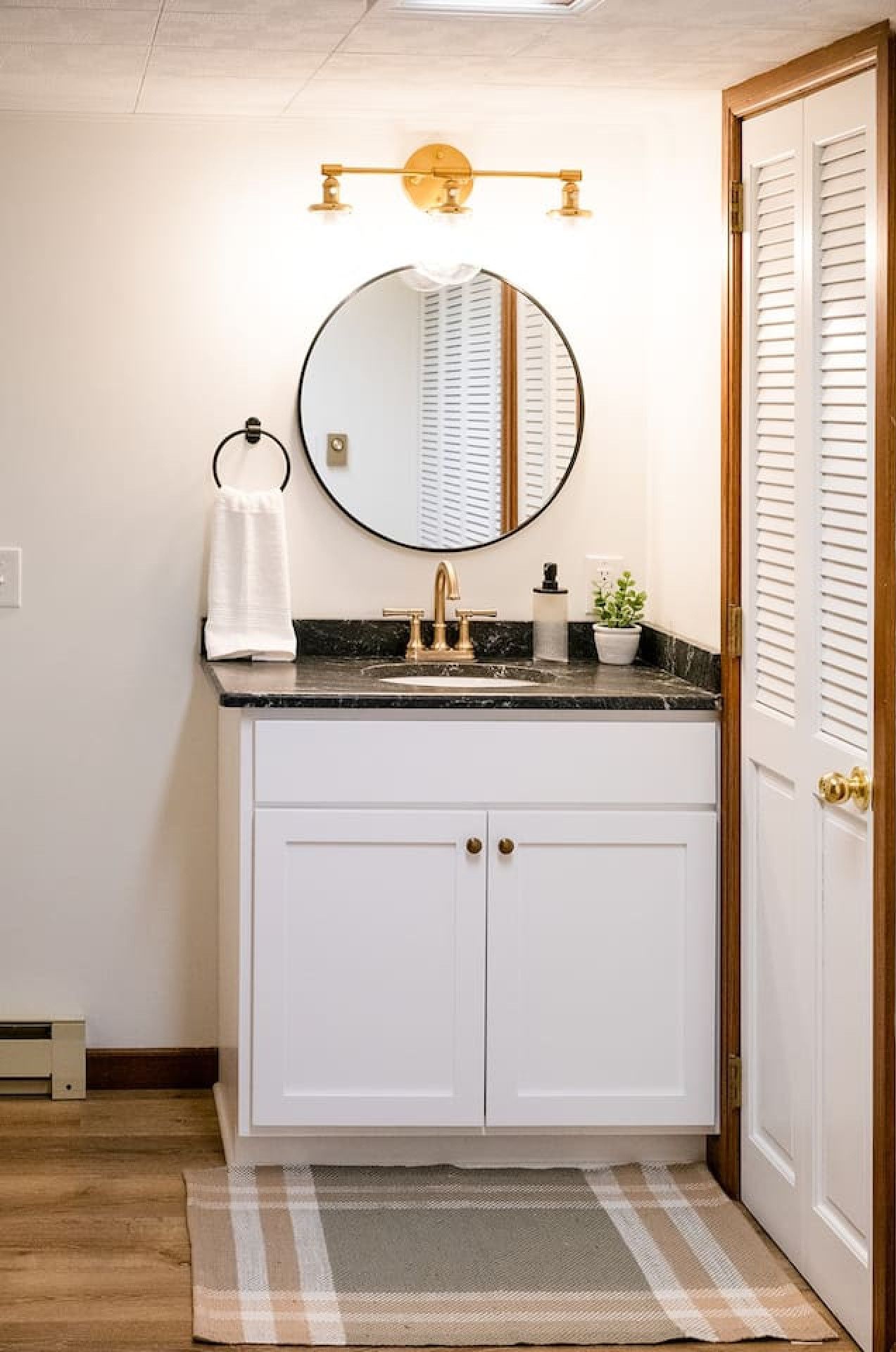 A bathroom with a white vanity, a round mirror, a gold faucet, and a towel ring.