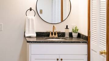A bathroom with a white vanity, a round mirror, a gold faucet, and a towel ring.