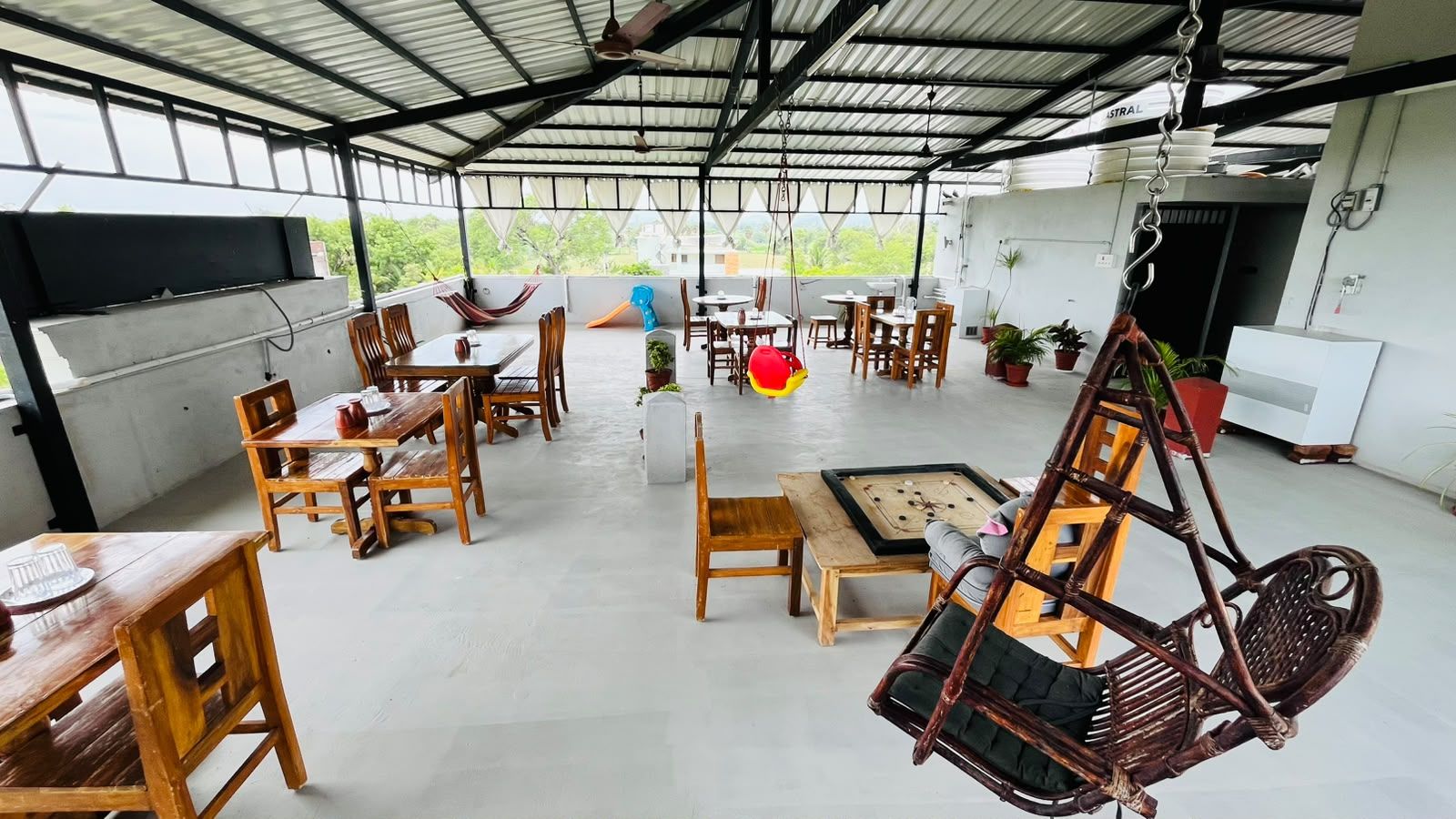 An open-plan dining area with wooden tables and chairs, a pool table, and a hanging chair.