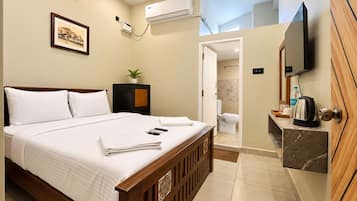 A hotel room with a bed, bedside table, air conditioning unit, a framed picture on the wall, and a television mounted on the wall.