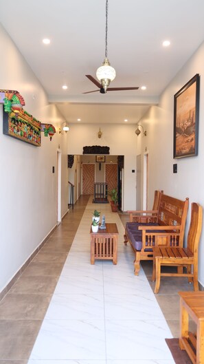 A hallway with a ceiling fan, a wooden bench, a small table with a plant, and a framed picture on the wall. - Dwaraka Resorts  (Tiruvannamalai)