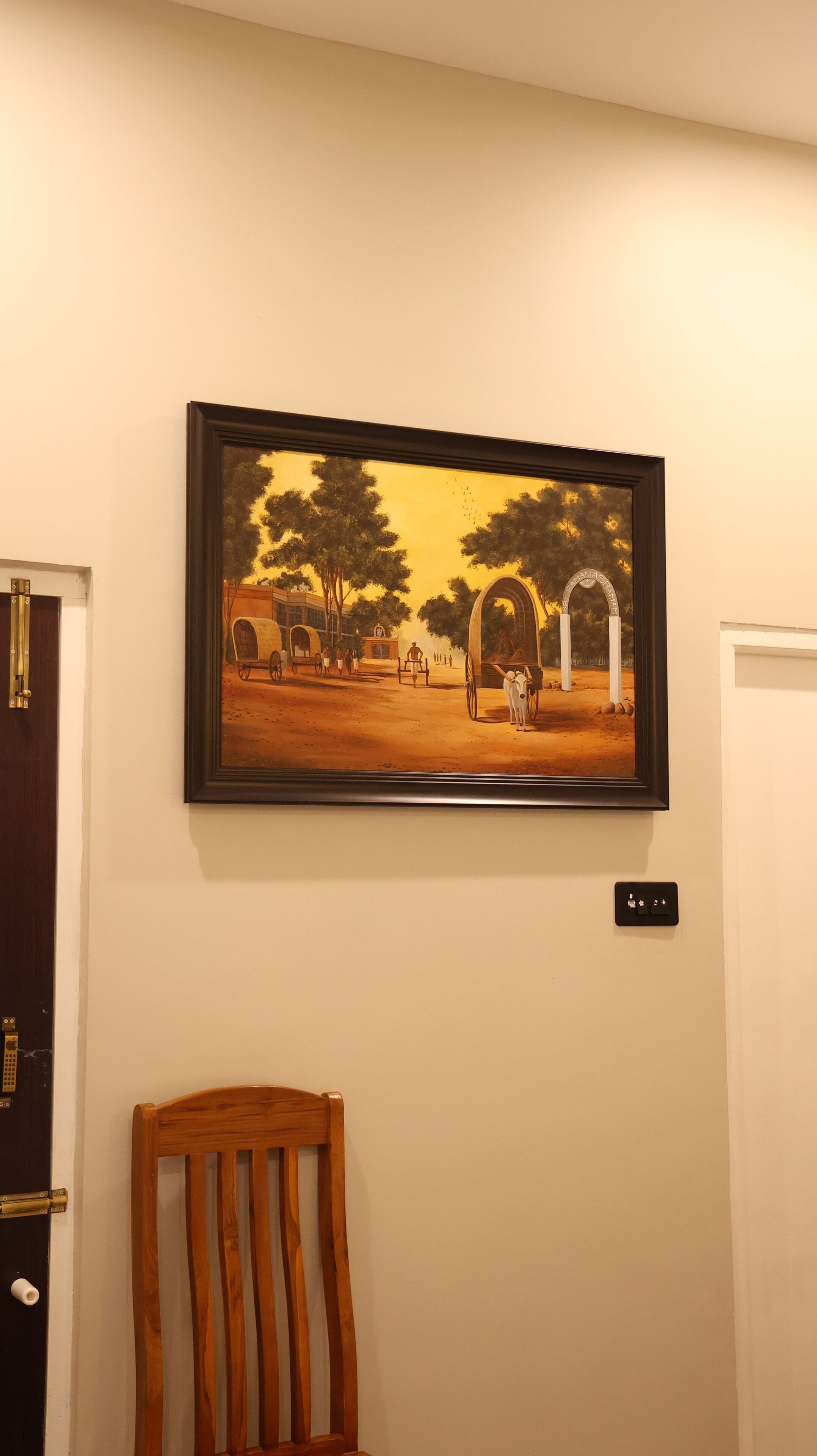 A framed painting of a rural scene with trees and a carriage on a wall.