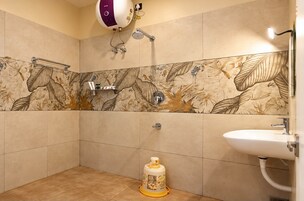 Un baño con ducha, inodoro y lavamanos, que cuenta con un salpicadero de azulejos con motivos florales y un dispensador de papel higiénico.