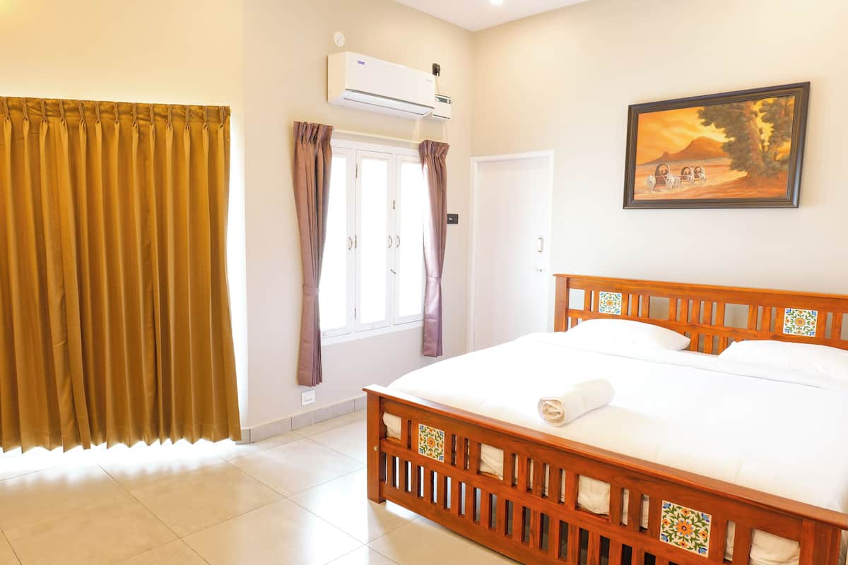Een slaapkamer met een bed, gordijnen, een airconditioning en een deur, plus een schilderij aan de muur.