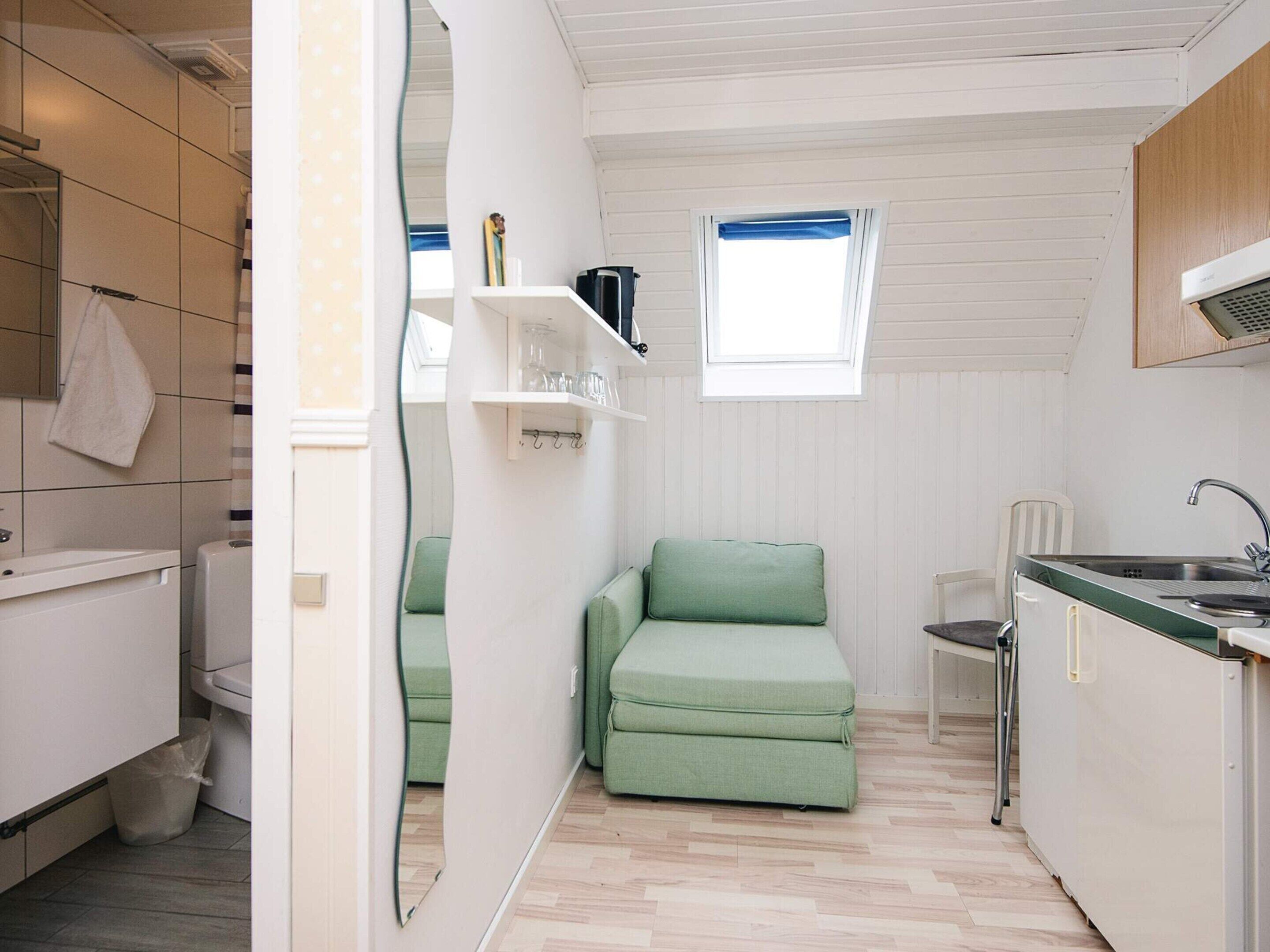 A compact kitchen with a green sofa, a small dining table, and a window with blue curtains.